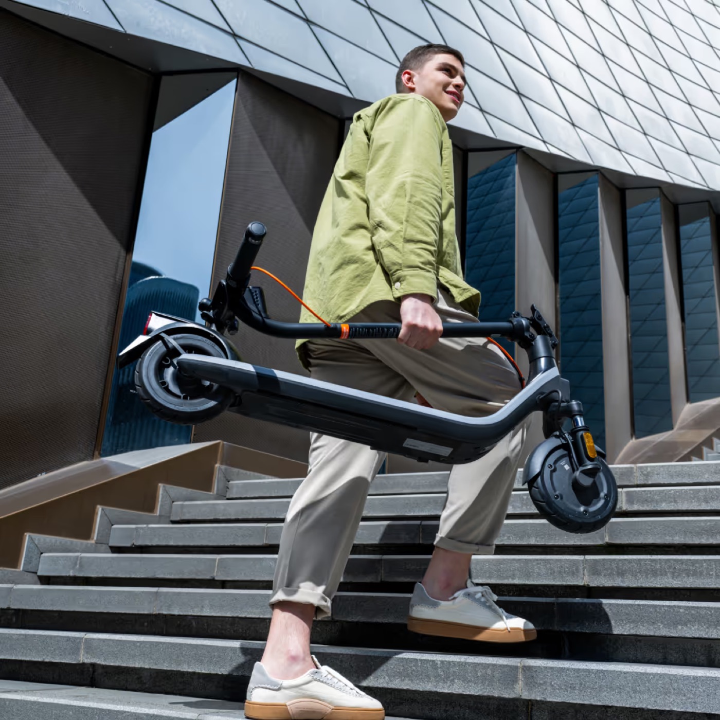 A man carrying a folded Segway Ninebot E2 Plus II up the stairs